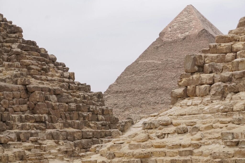 منظر قريب للأهرامات المصرية في الجيزة، يُظهر تفاصيل الأحجار الضخمة المكدسة بدقة مذهلة، مع رؤية هرم خفرع في الخلفية وأجزاء من الأهرامات الأصغر في المقدمة