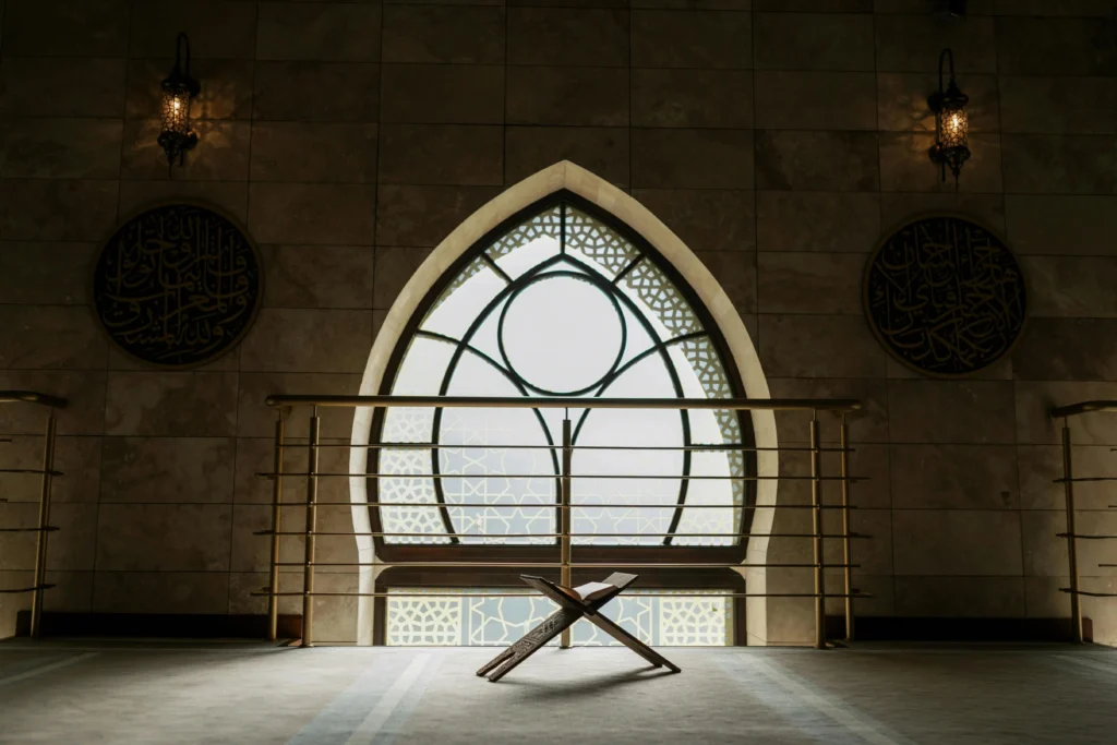 نافذة قِبلة مزخرفة بإطار حجري ودرابزينٍ معدني تطل على سماء مزدحمة بالسحب، تعكس جمال فن العمارة الإسلامية.