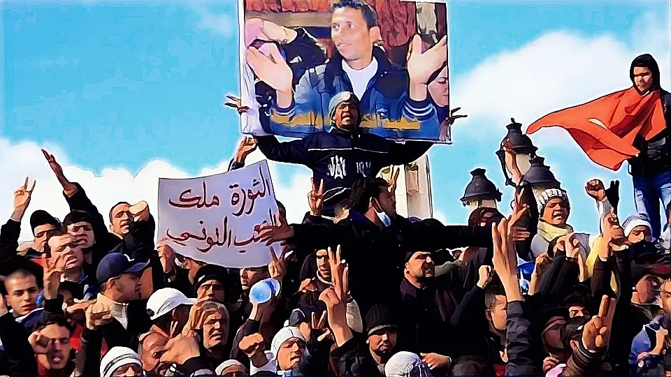 متظاهرون يحملون لافتات وصورة محمد البوعزيزي خلال إحدى مظاهرات الربيع العربي في تونس، تعبيراً عن الغضب الشعبي والمطالبة بالتغيير.