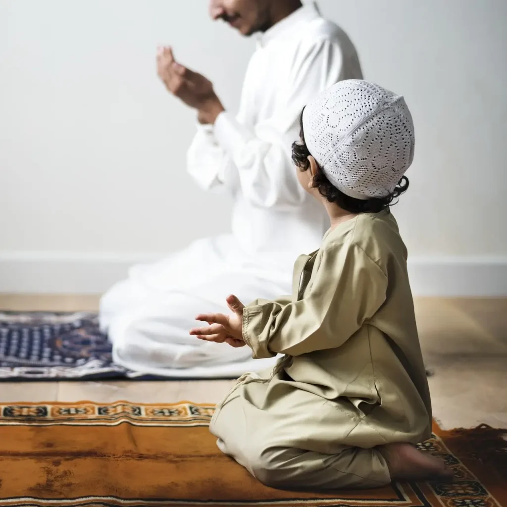 طفل صغير يرتدي لباسًا تقليديًا ويقلد والده أثناء الصلاة، في مشهد يعكس القدوة الإيمانية والروحية داخل الأسرة.
