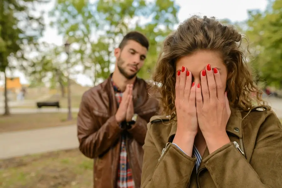 امرأة تقف خلف رجل في لحظة توتر وصمت، تُوحي بموقف عاطفي أو خلاف بين طرفين