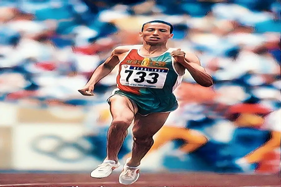 سعيد عويطة أثناء سباق أولمبي يرتدي زي المنتخب المغربي، يركض بثبات في إحدى لحظات المجد.