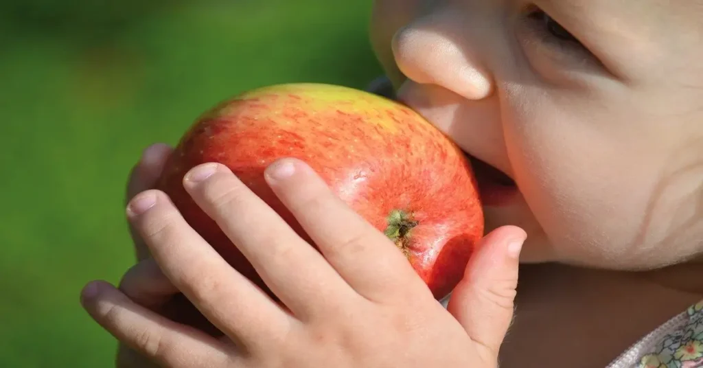 طفل سعيد يأكل تفاحة طازجة، رمزية للمناعة القوية والحماية الطبيعية.