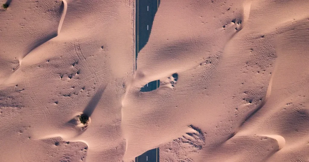 طريق مغطى بالرمال وسط منطقة صحراوية يرمز إلى التصحر في الوطن العربي