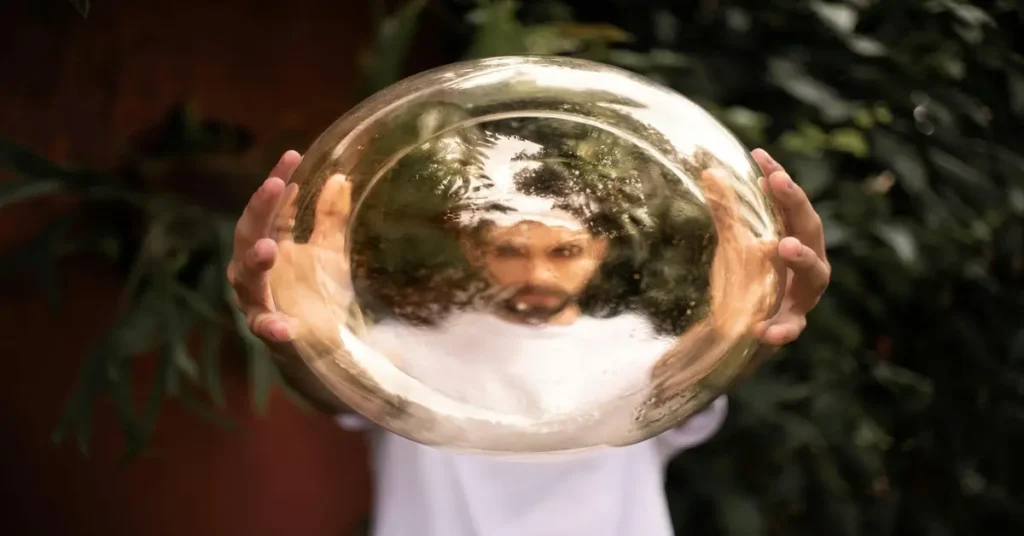 رجل يحمل كرة شفافة تعكس ملامحه بشكل غير واضح، رمز يوضح أن الأفعال تكشف الحقيقة أكثر من الكلمات.