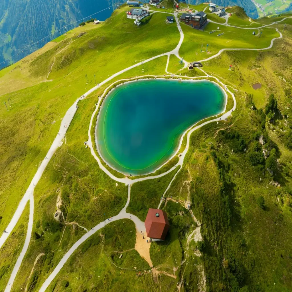 لقطة جوية لبحيرة جبلية صافية محاطة بالجبال الخضراء في يوم صيفي مشمس.