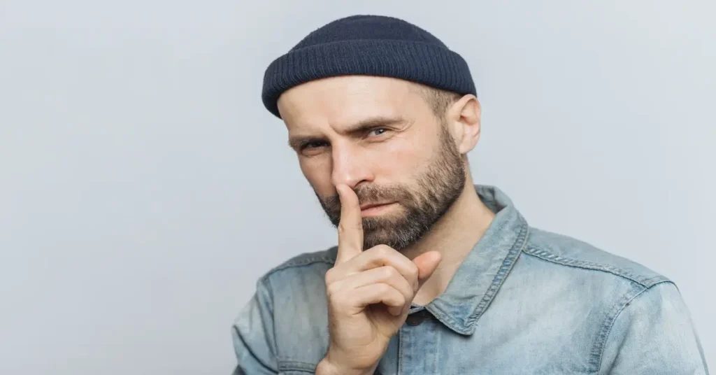 رجل يضع إصبعه على شفتيه في إشارة للصمت، يرمز إلى خطورة اللسان وكلمات الوشاية التي قد تؤذي الآخرين.