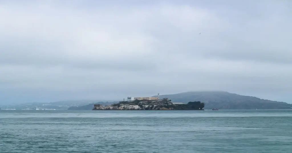 منظر عام لجزيرة ألكاتراز وسجنها الشهير في خليج سان فرانسيسكو، محاطة بالمياه والضباب، ترمز إلى العزلة والحراسة المشددة لسجن "الصخرة" الذي شهد عملية الفرار الأكثر غموضاً.