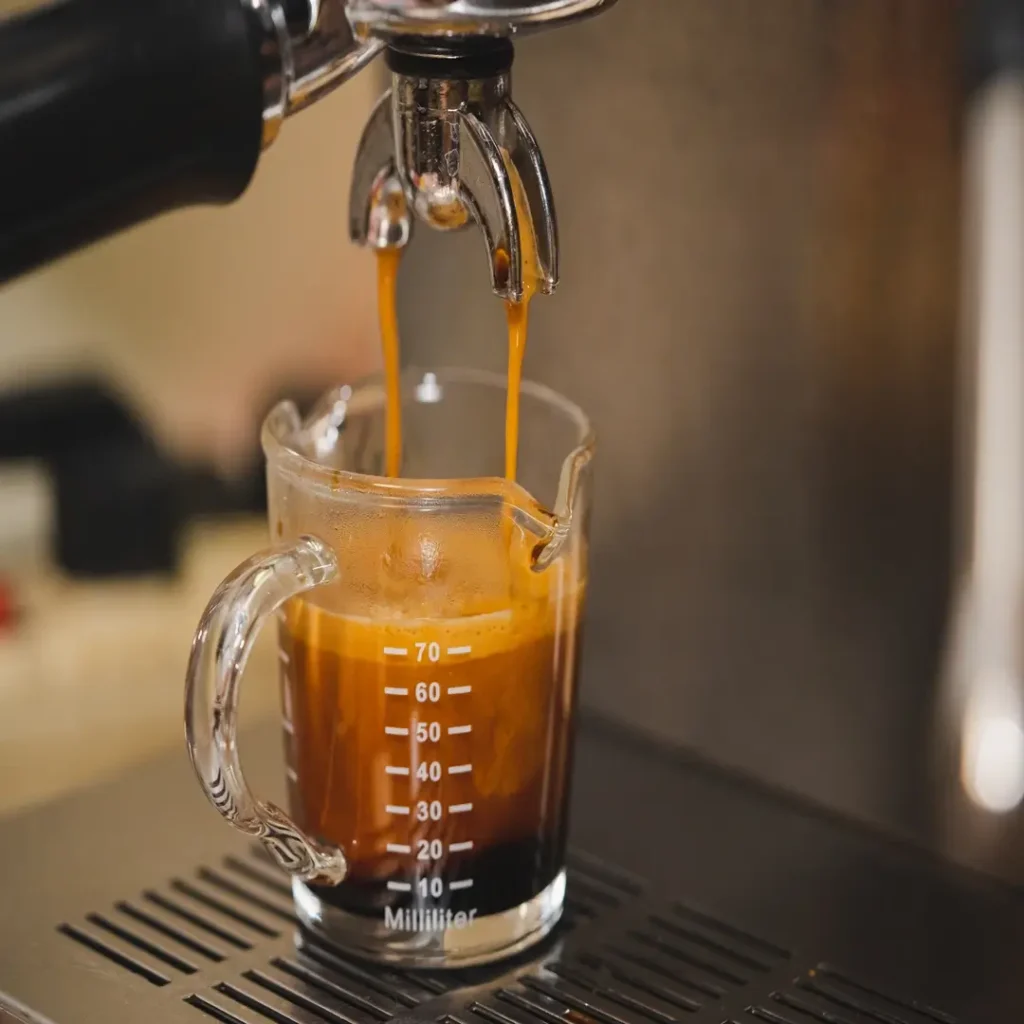 استخلاص لقطة إسبريسو طازجة تتدفق في كوب زجاجي صغير داخل ماكينة القهوة