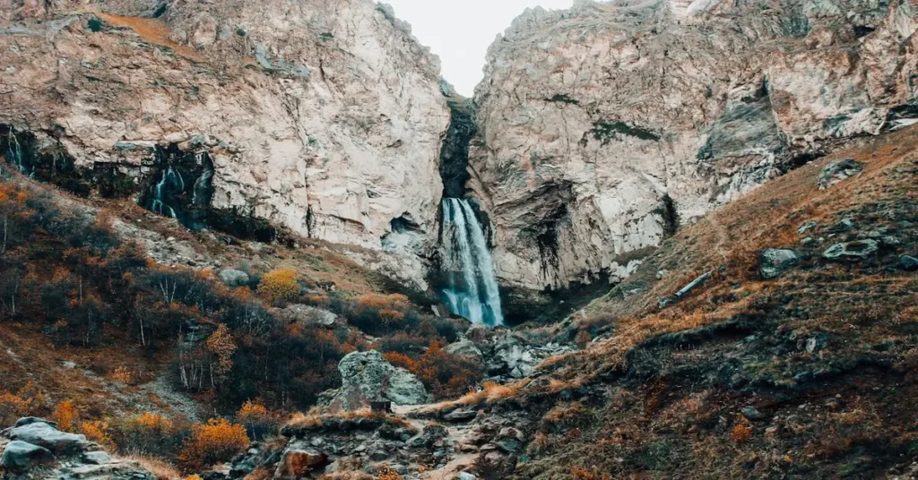 شلال يتدفق من بين الصخور الجبلية، يرمز إلى حركة المياه الجوفية وتغذيتها للطبيعة في أعماق الأرض.